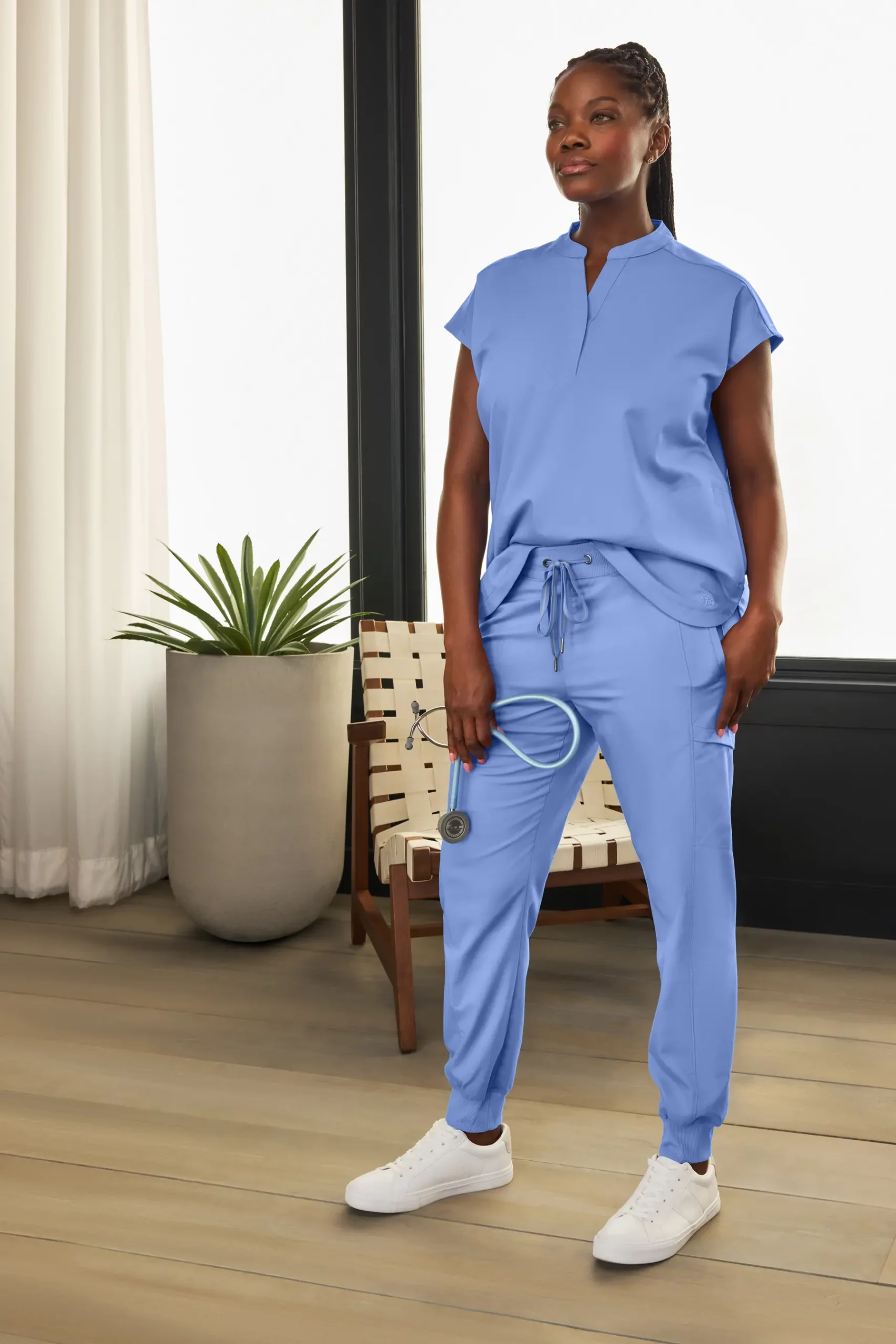 Healthcare professional wearing blue scrubs from the Kilato collection, standing confidently in a modern interior