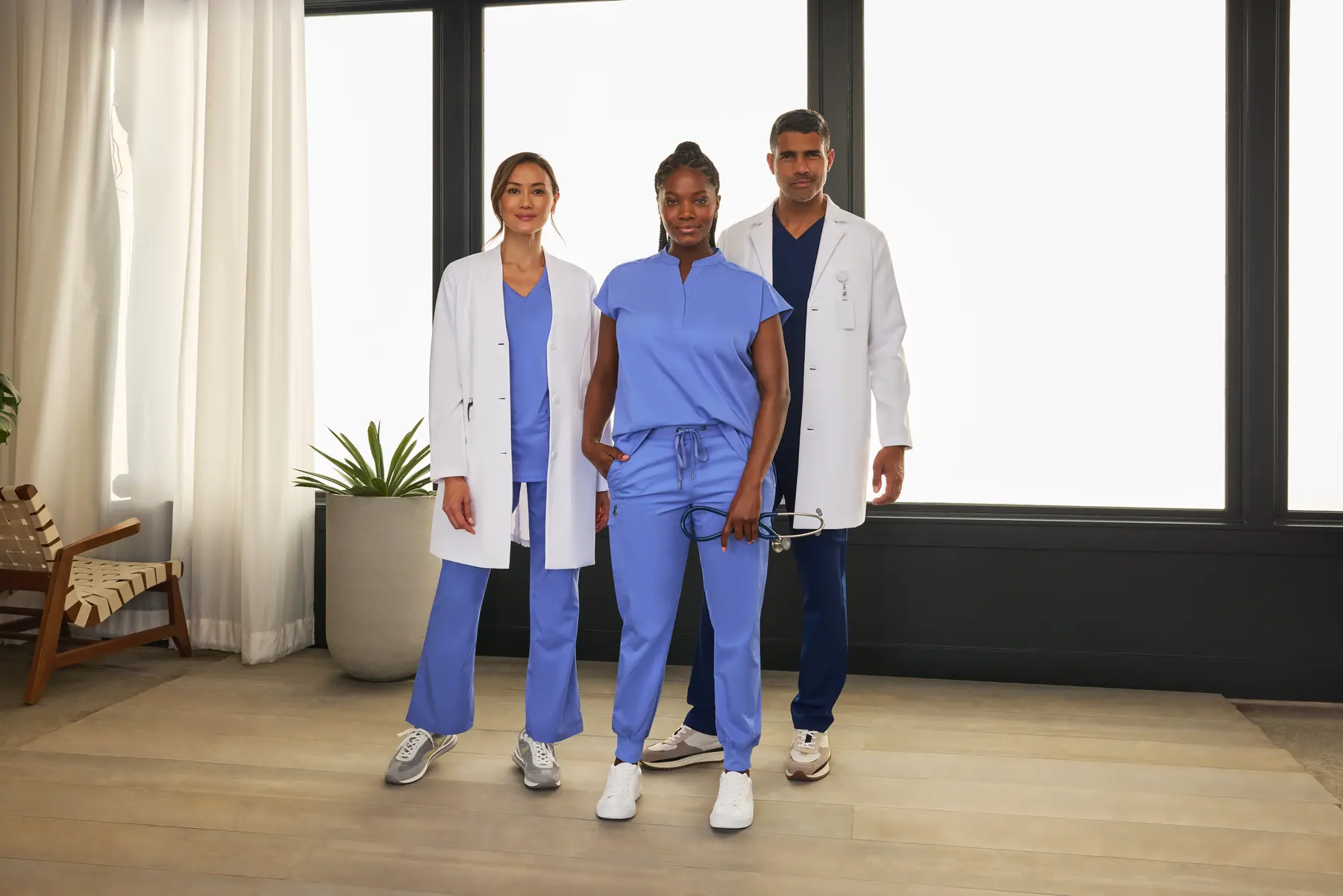 Three healthcare professionals in lab coats and scrubs standing together in a modern medical environment.