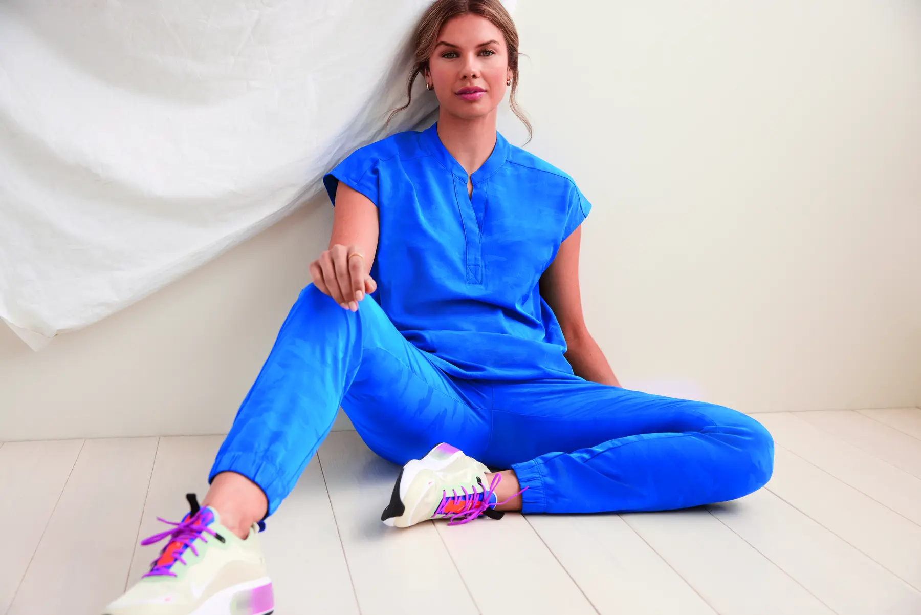 Healthcare professional in bright blue scrubs sitting on the floor, illustrating comfort and approachability.
